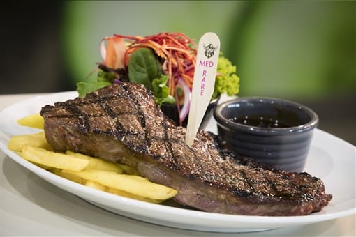 A steak with chips and a pot of sauce